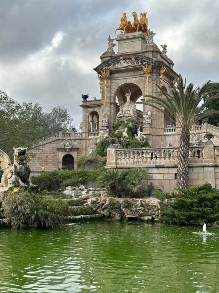 Triumphal Arch and fountain with ornate golden chariots, sculptures, and a dragon statue in a Barcelona park.