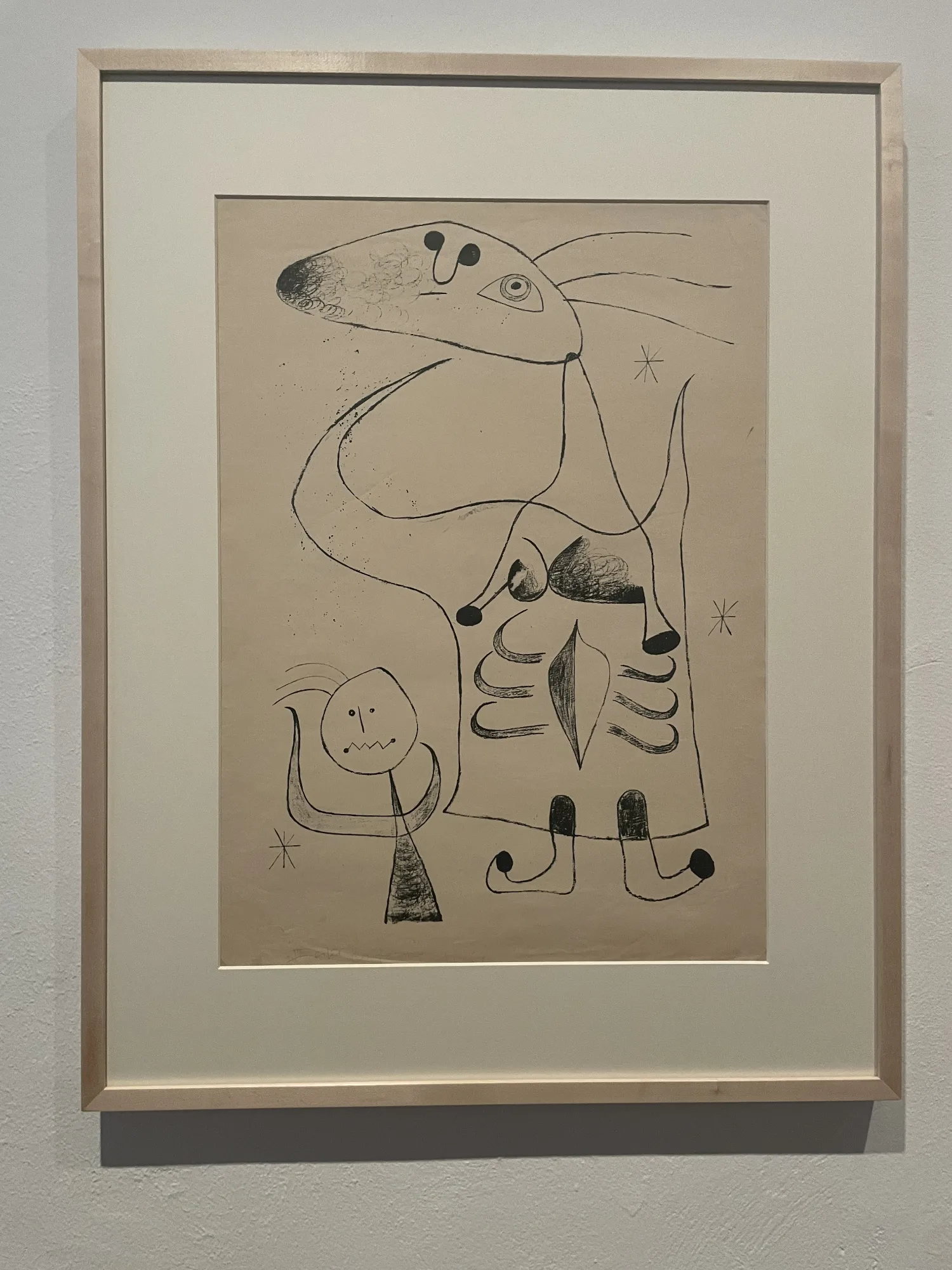 Framed black line drawing by Joan Miró, featuring abstract figures on a light beige background, displayed in a museum.