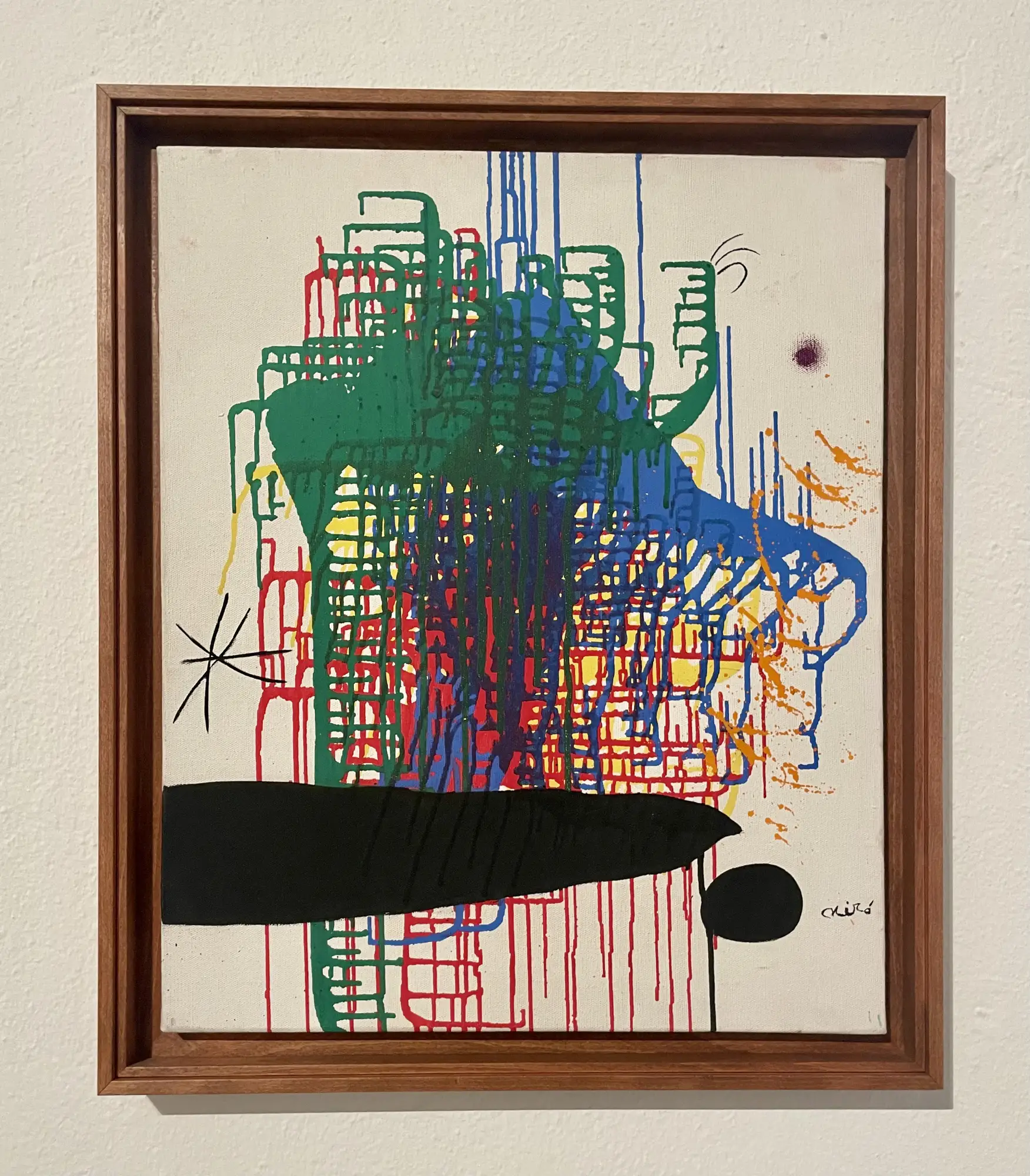 Vibrant abstract painting by Joan Miró, featuring dripping primary and secondary colors over a white canvas, within a wooden frame.