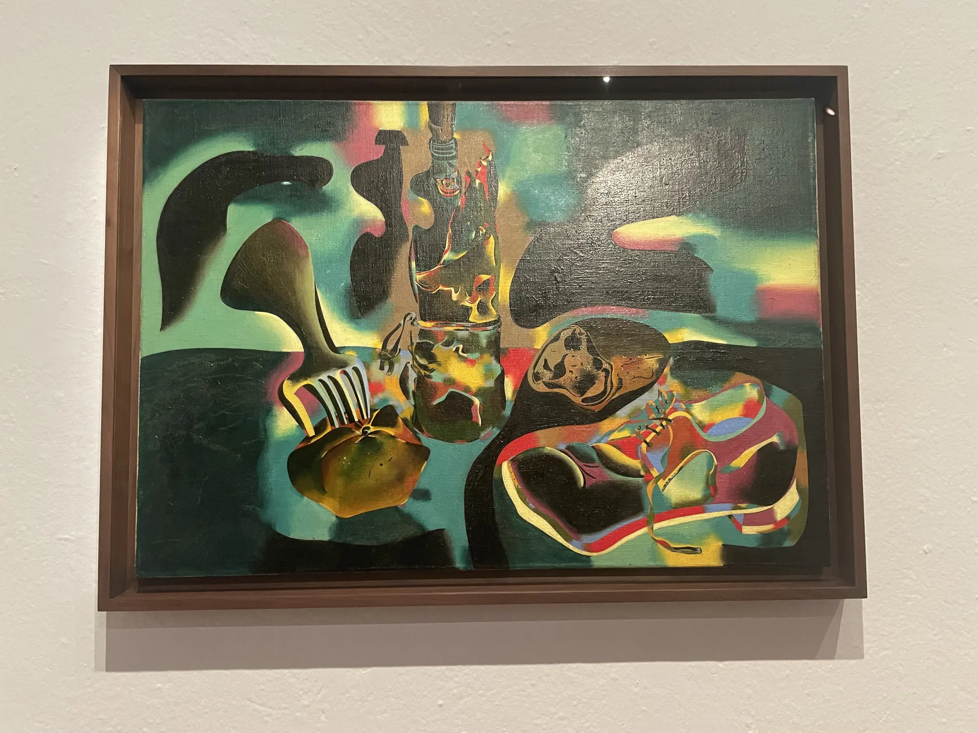 Colorful surrealist still life painting with a fork, bottle, and fruit on a dark background, in a museum exhibit.