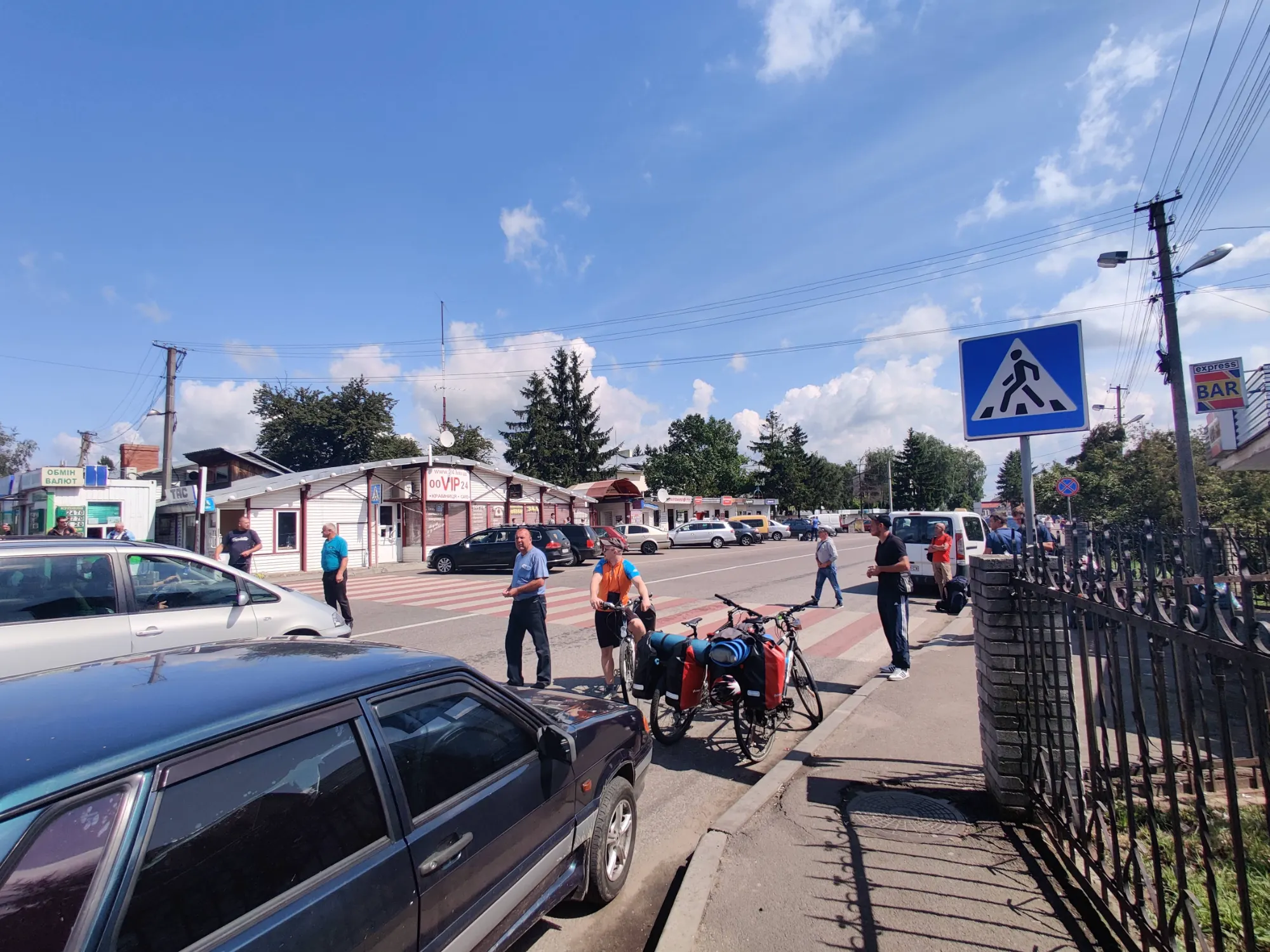 Piesi i rowerzyści czekający na przejściu granicznym Szeginie między Ukrainą a Polską w słoneczny dzień.