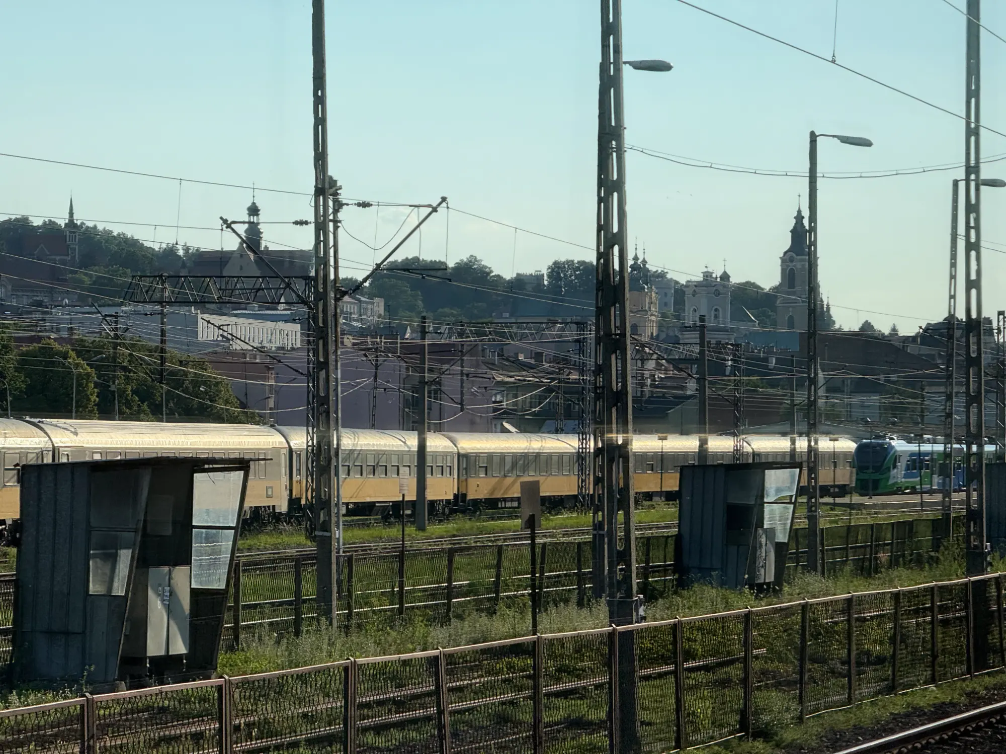 Pociąg pasażerski przejeżdża obok torów stacji Przemyśl Główny, w tle widać wieże zabytkowego kościoła.