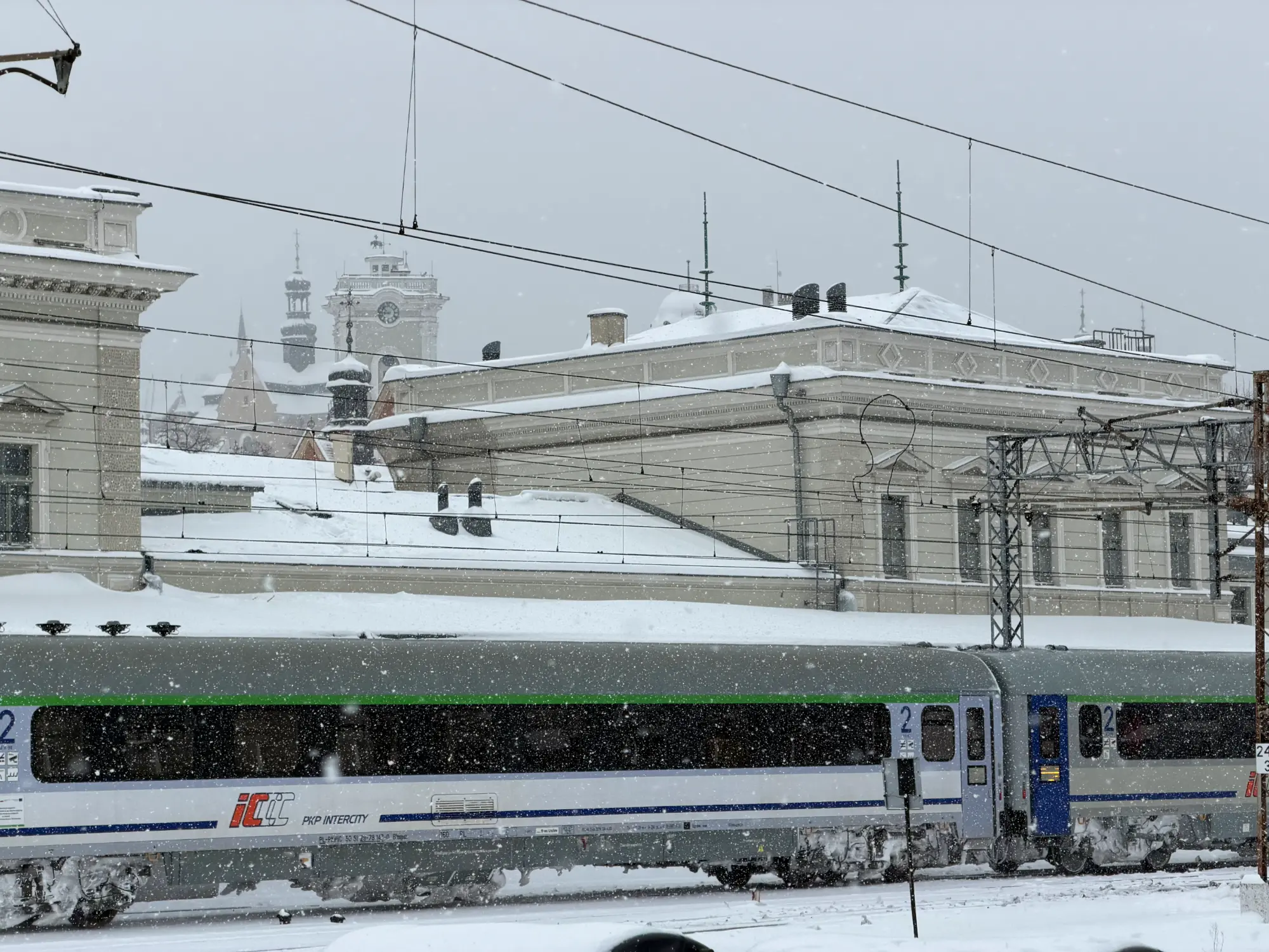 Pociąg PKP Intercity na zaśnieżonej stacji w Przemyślu, w tle zabytkowa architektura.