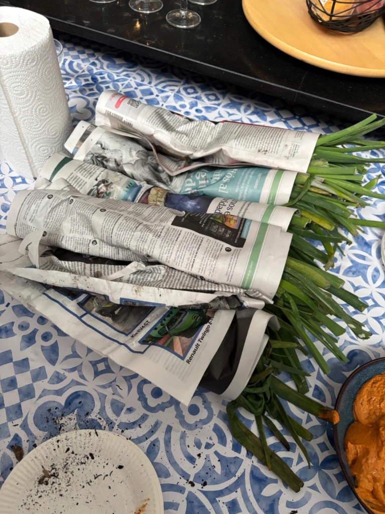 Manojos de calçots asados envueltos en papel de periódico para mantener el calor, sobre una mesa de azulejos azules.