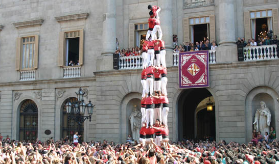 Castellers build a human tower in front of Barcelona City Hall at Plaça Sant Jaume surrounded by a crowd.