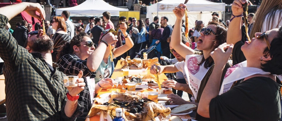 Grupo de personas al aire libre comiendo calçots, sosteniéndolos en alto, una estampa típica de la tradición catalana.