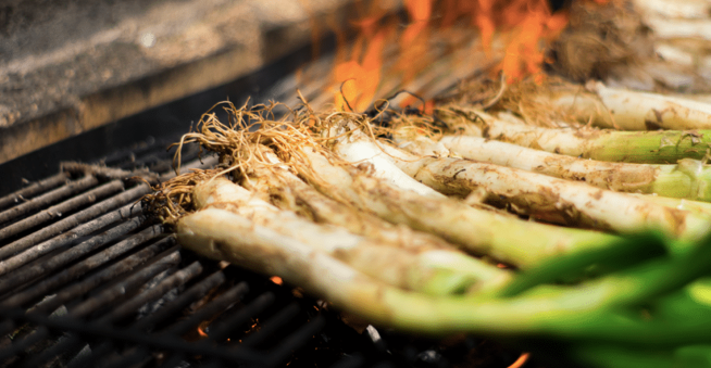 Close-up of calçots, traditional Catalan green onions, grilling over an open flame on a barbecue grate.