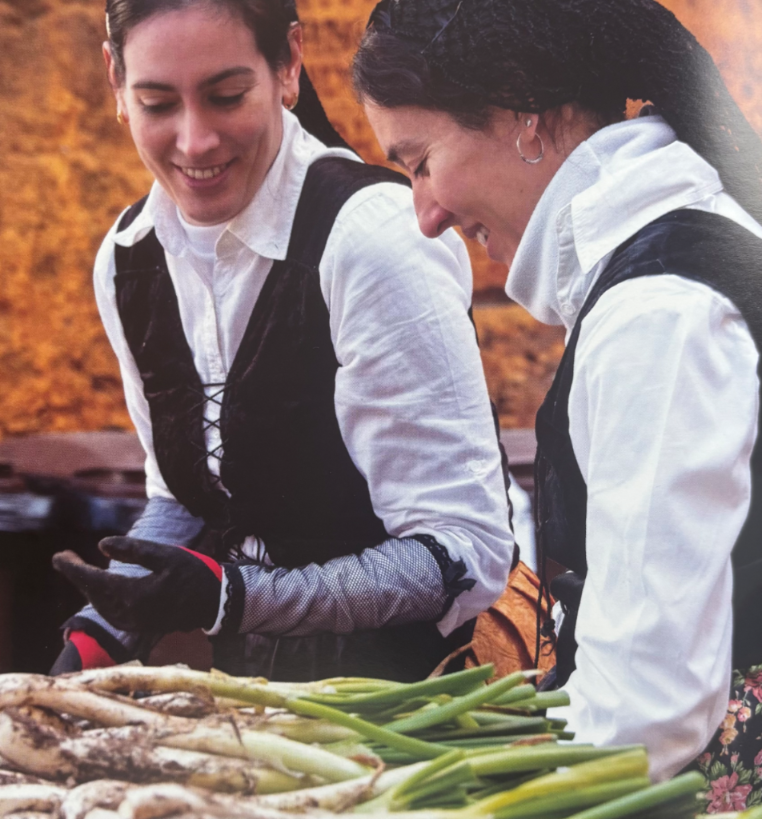 Two smiling women in traditional dress arranging piles of calçots, typical Catalan green onions.