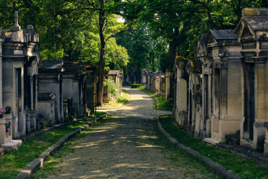 Cobblestone path lined with stone tombs and large trees at Père Lachaise Cemetery in Paris.