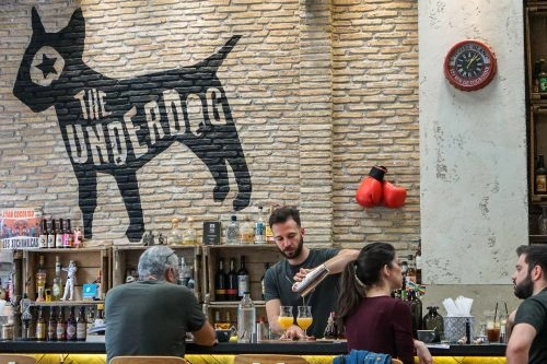 Barista at The Underdog bar in Athens with a large black dog mural on the brick wall.