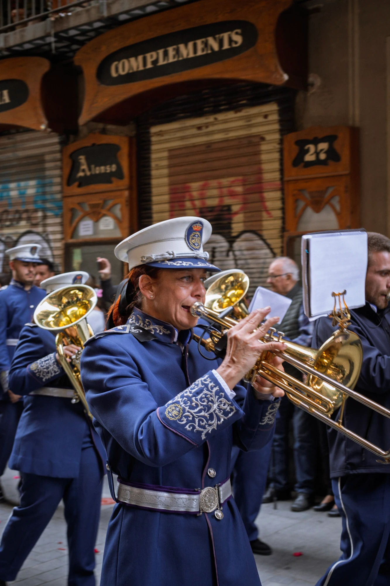 Woman in a blue uniform playing a trumpet in a marching band during a street parade in Barcelona.