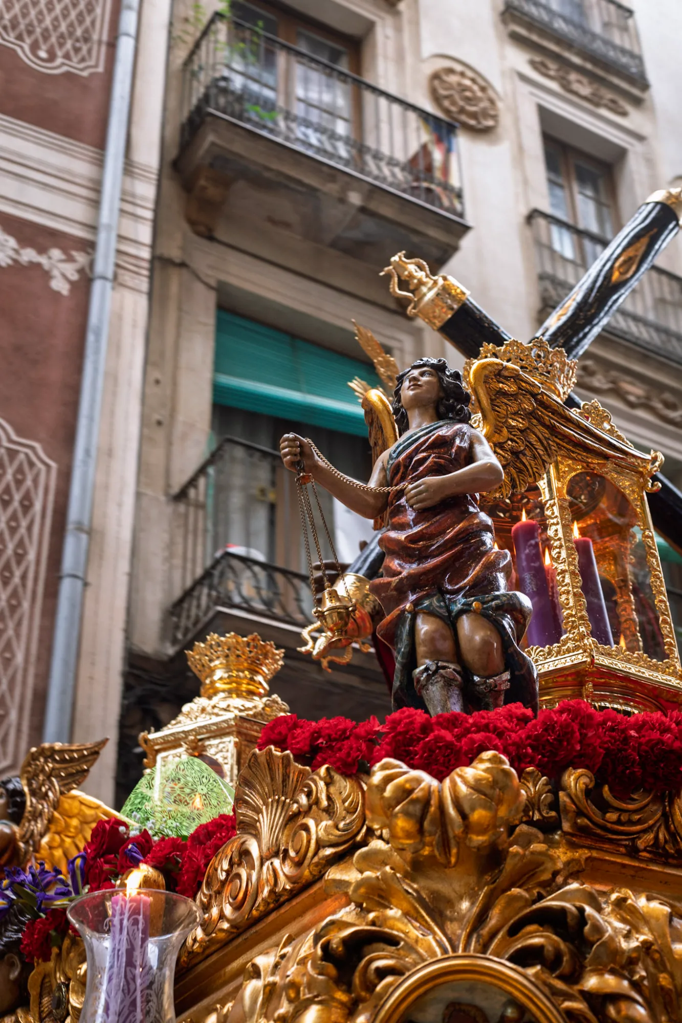 Close-up of an angel statue on a golden religious float decorated with red carnations during a procession in Barcelona.