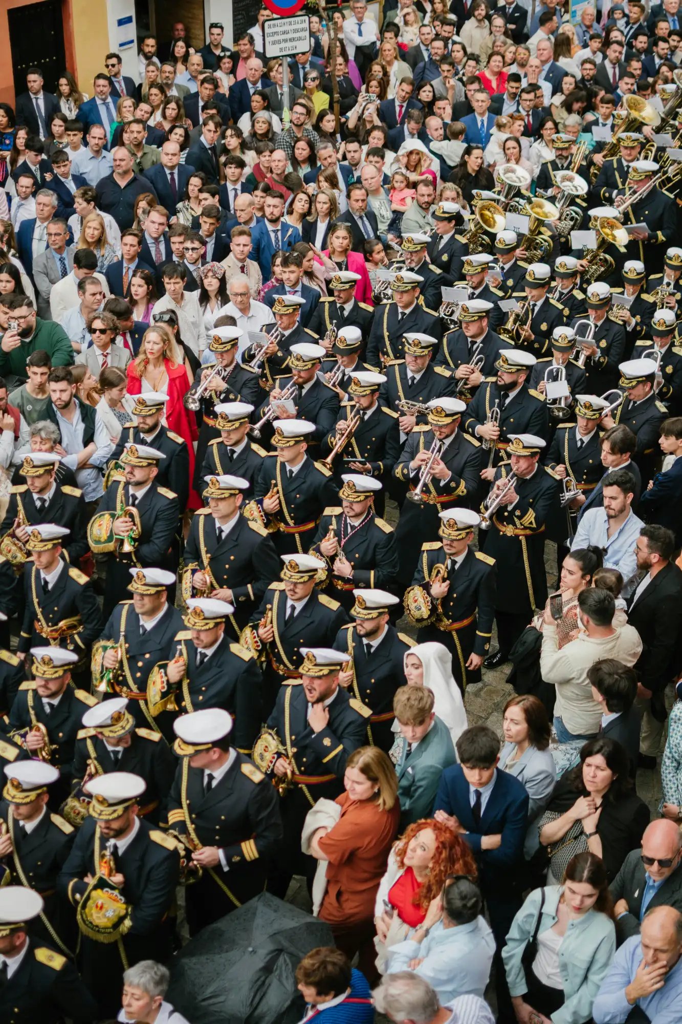 A marching band in dark uniforms and white hats plays brass instruments while walking through a dense crowd in Madrid.