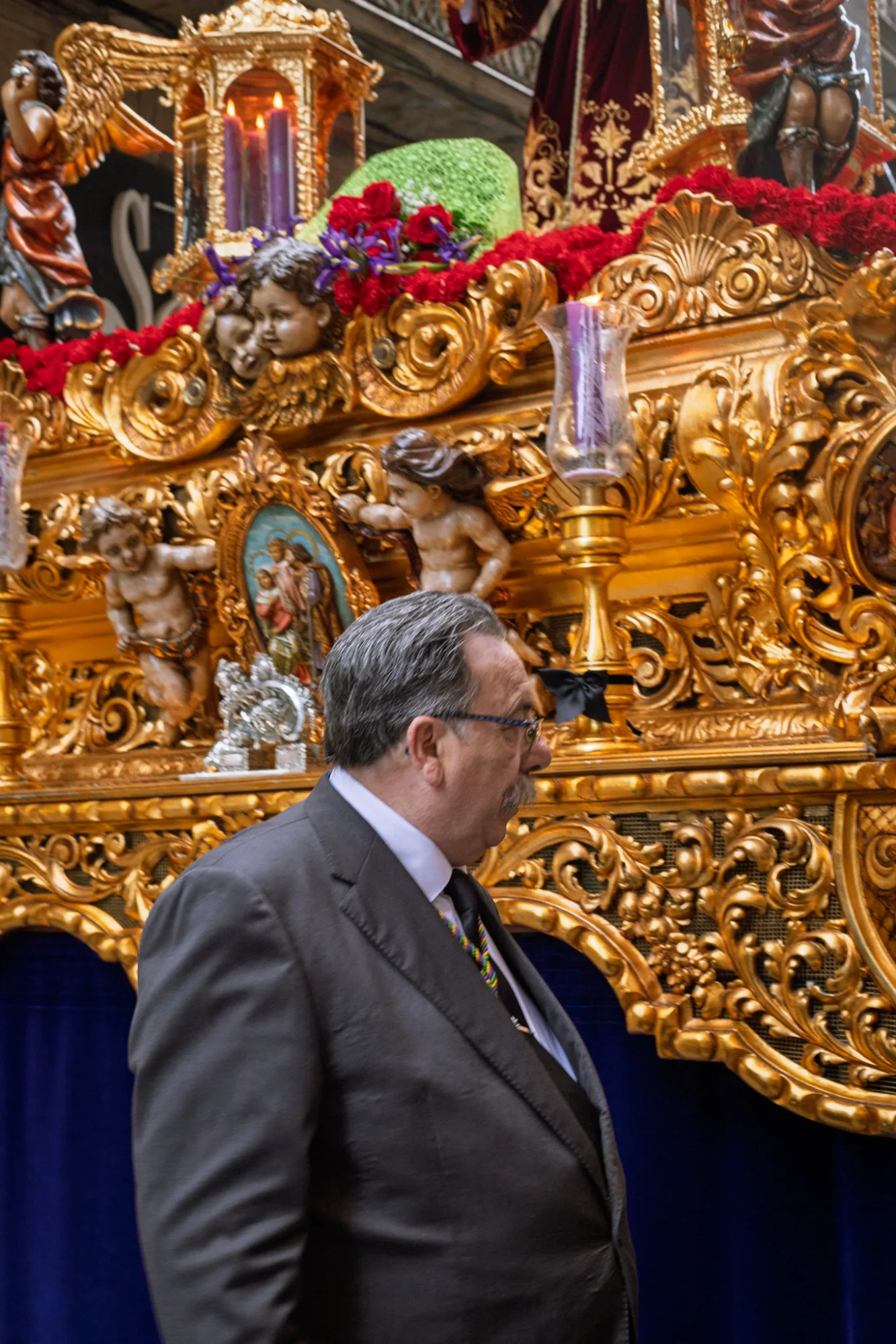 Man in a suit standing by an ornate gold religious float decorated with flowers and cherubs during a procession in Barcelona.