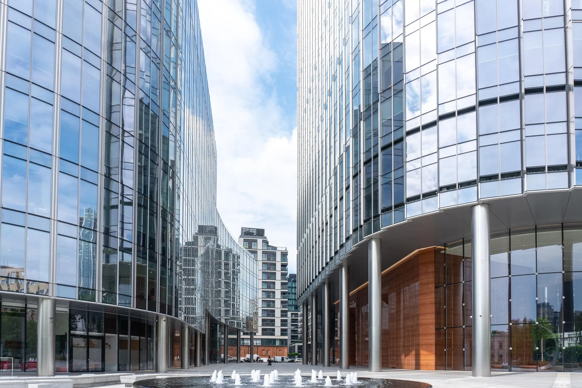Curved glass facades of modern office buildings at Plac Europejski in Warsaw with ground-level fountains.