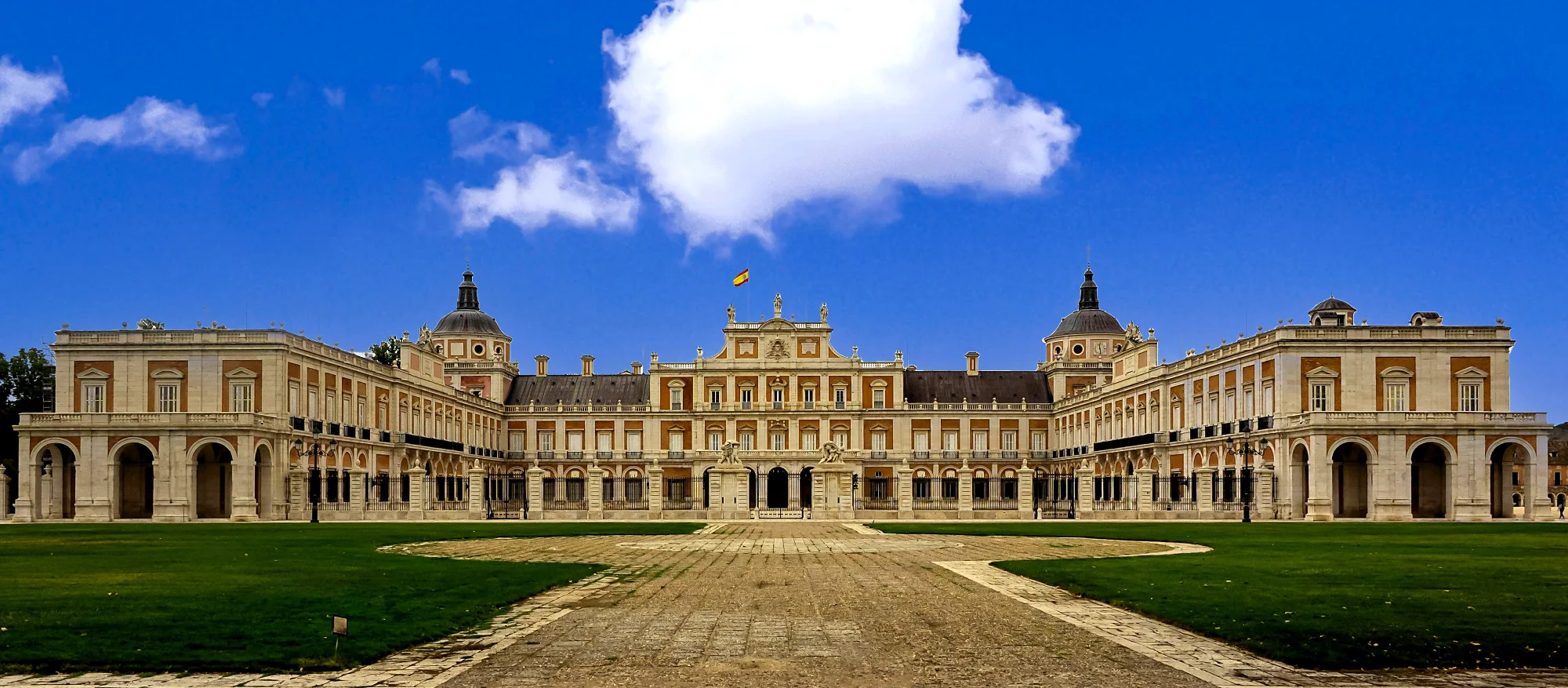 Front view of the Royal Palace of Aranjuez in Spain, featuring a symmetrical red brick and white stone facade.