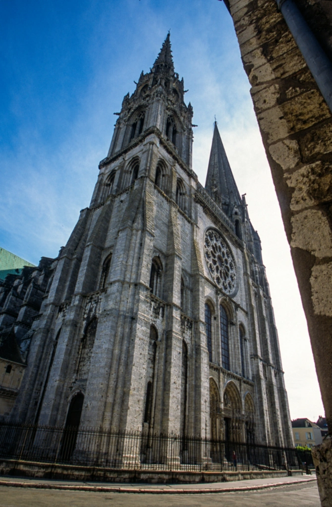 Chartres Cathedral featuring its distinct asymmetrical spires, rose window, and Gothic stone facade against a blue sky.