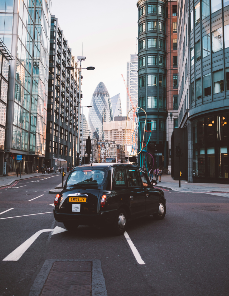 Black cab driving on a London street with the Gherkin building visible in the background.