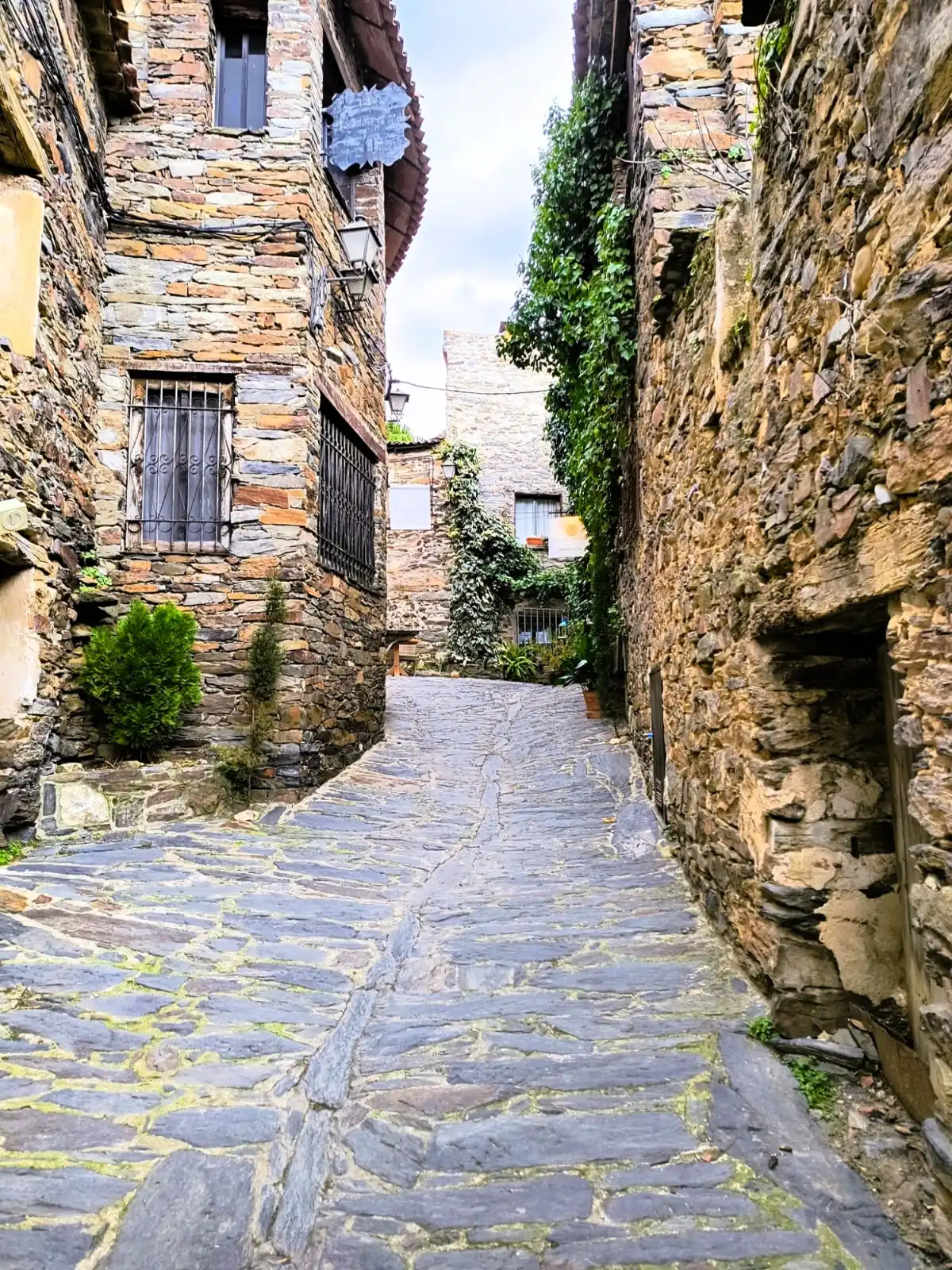 Cobblestone street lined with traditional dark slate stone houses in Patones de Arriba, Spain.