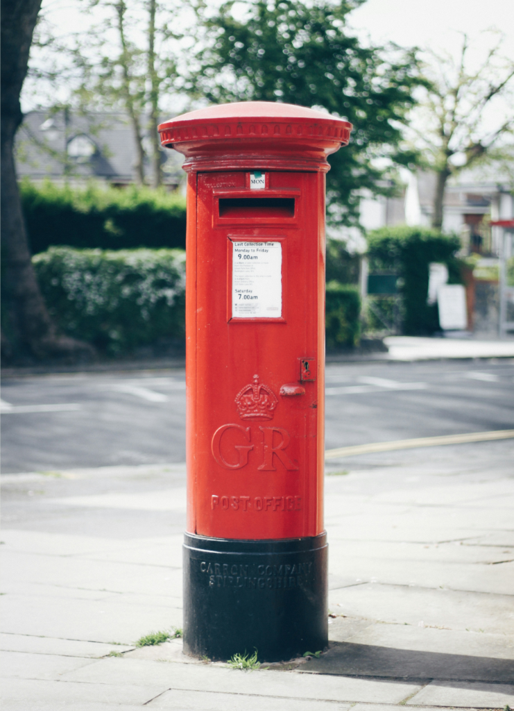 A traditional red British pillar postbox with a GR royal cipher standing on a paved sidewalk.