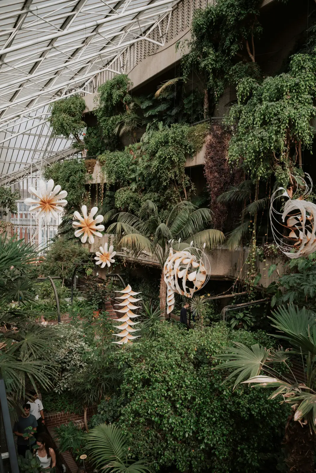 The lush interior of the Barbican Conservatory in London, with tropical plants growing over Brutalist concrete balconies.