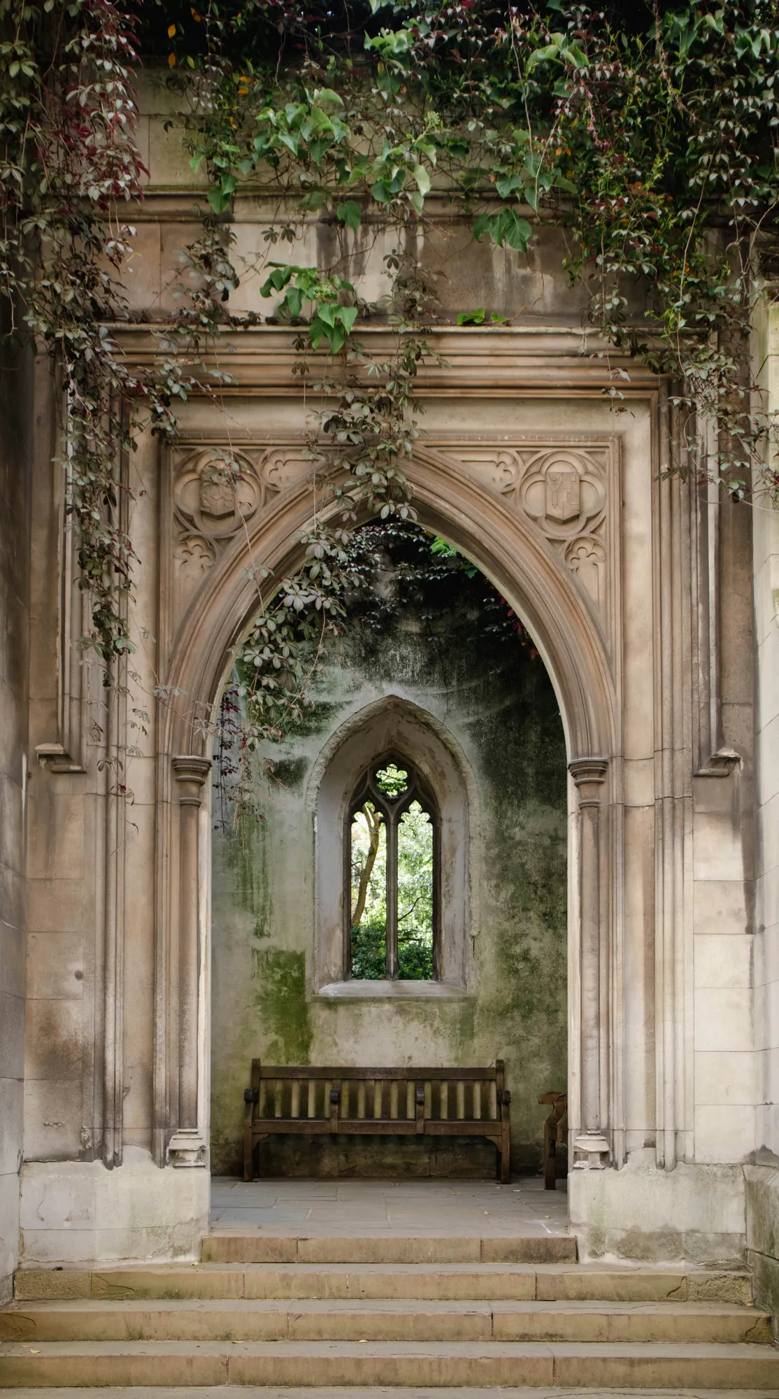 A Gothic stone archway covered in ivy inside the ruins of St Dunstan-in-the-East church in London.
