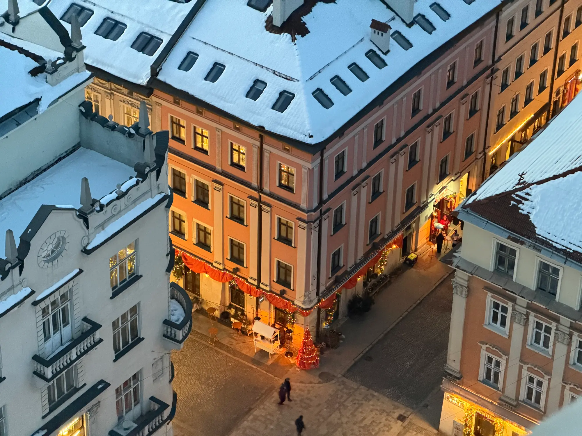 An overhead view of a snowy street corner in Lviv's Old Town at dusk, with Christmas lights and decorations.